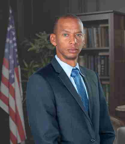 A man wearing a suit standing inside a courtroom with the flag of United Stated in the background